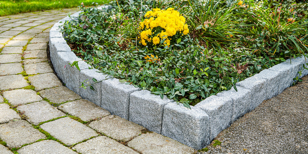 Beuta Greystone block edging surrounds a flower bed with yellow flowers.